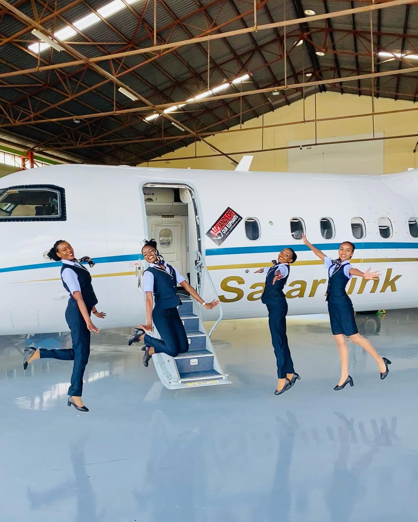 Safarilink cabin crew jumping beside a Dash 8 aircraft in the hangar